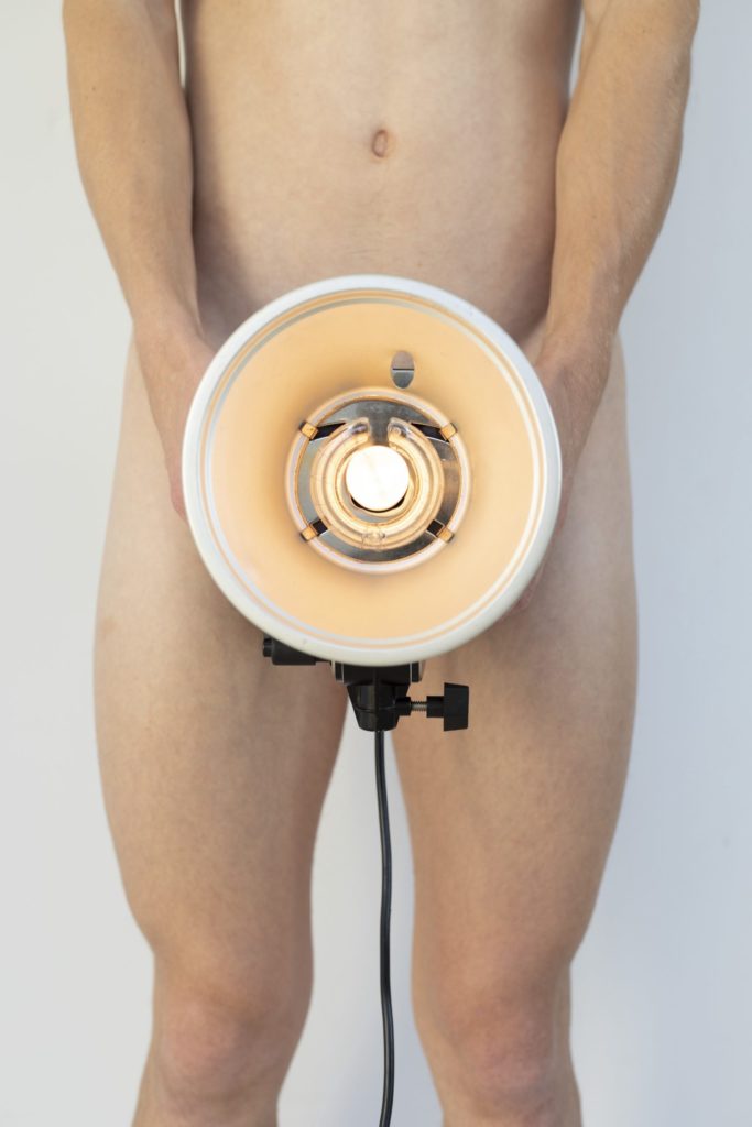 An artistic photograph of a man holding a lit lamp over his hips.